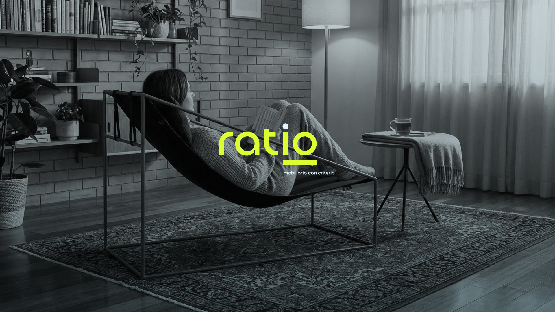 Person reading in a Ratio chair, in a black-and-white living room with a blue tint